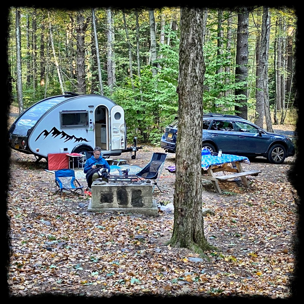 A view of the T@B and campsite sitting by the fire with leaves on the ground