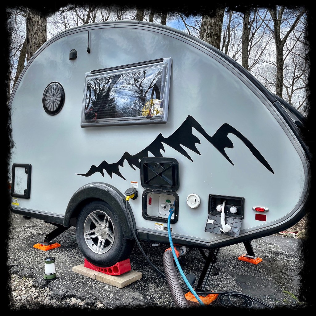 Picture of the open Nautilus hatch with water line plugged in and sewer hose plugged in below. Outdoor shower cabinet is also open. 