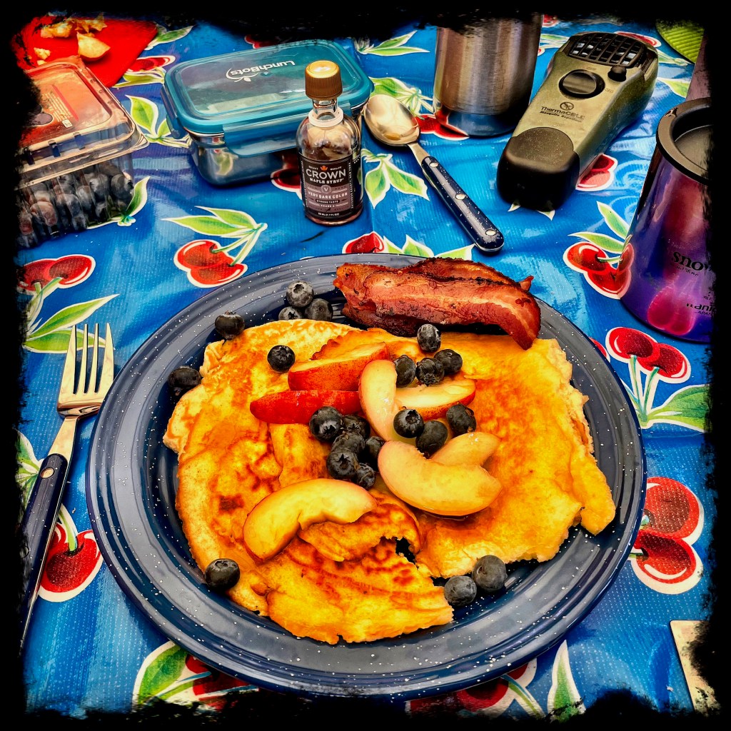 Pancakes with peaches and blueberries on an enamel camping plate