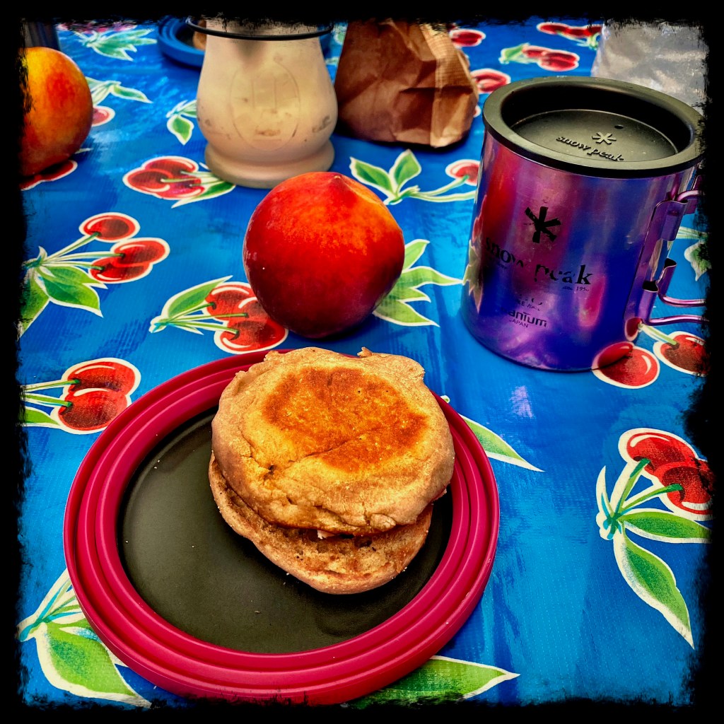 Plate with english muffin breakfast sandwich, peach and coffee