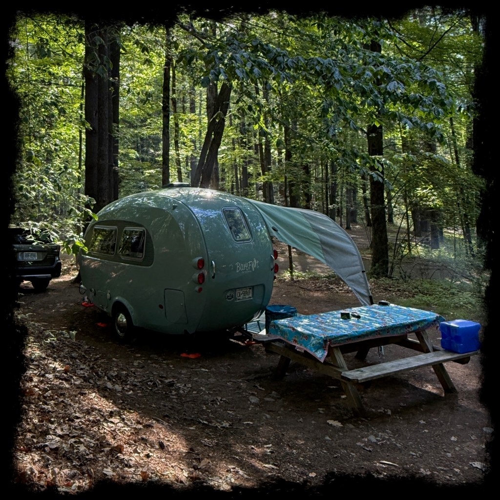 Barefoot Caravan with an awning attached and next to a picnic table with a blue cloth. 